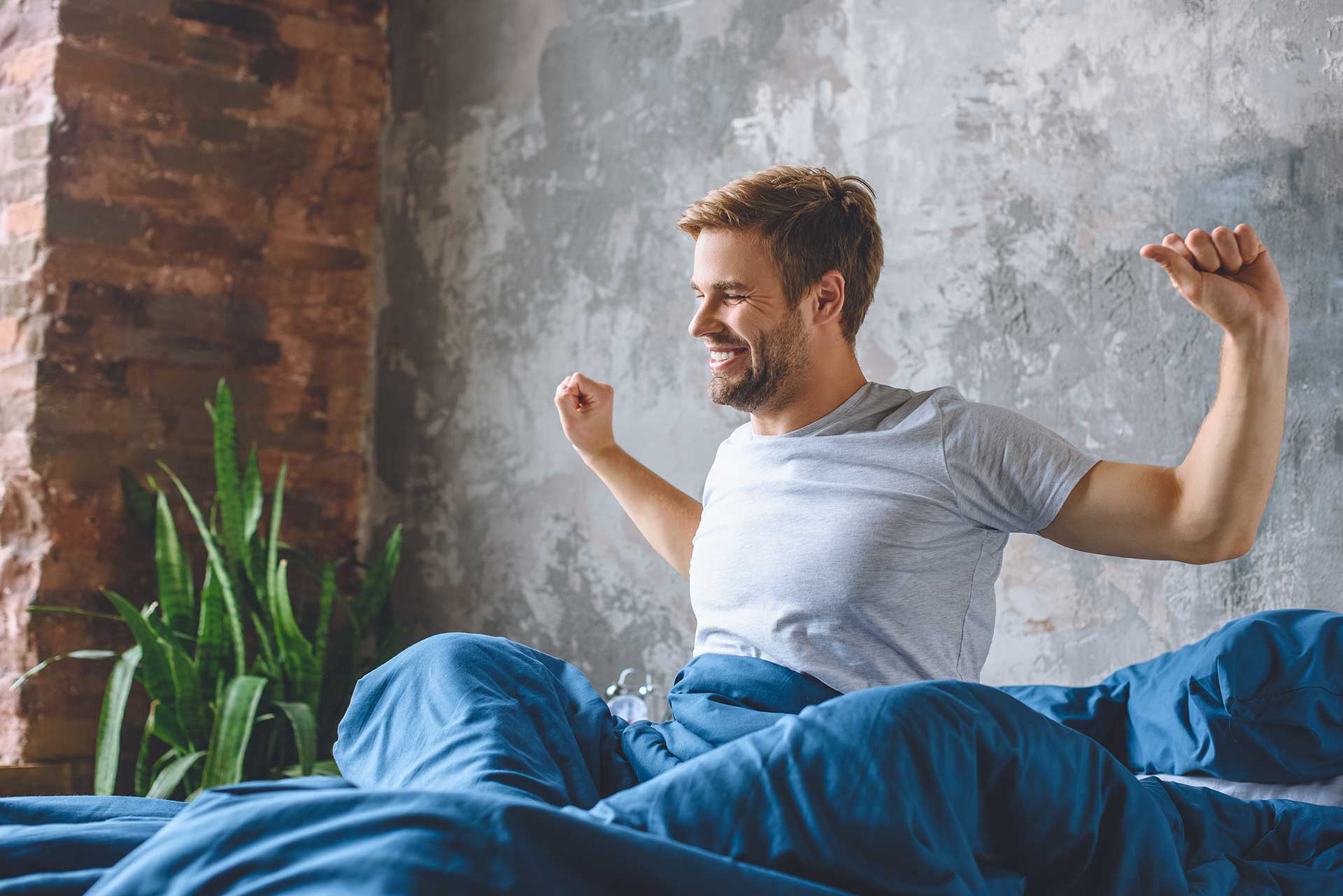 Handsome young man stretching in bed during morning time at home.