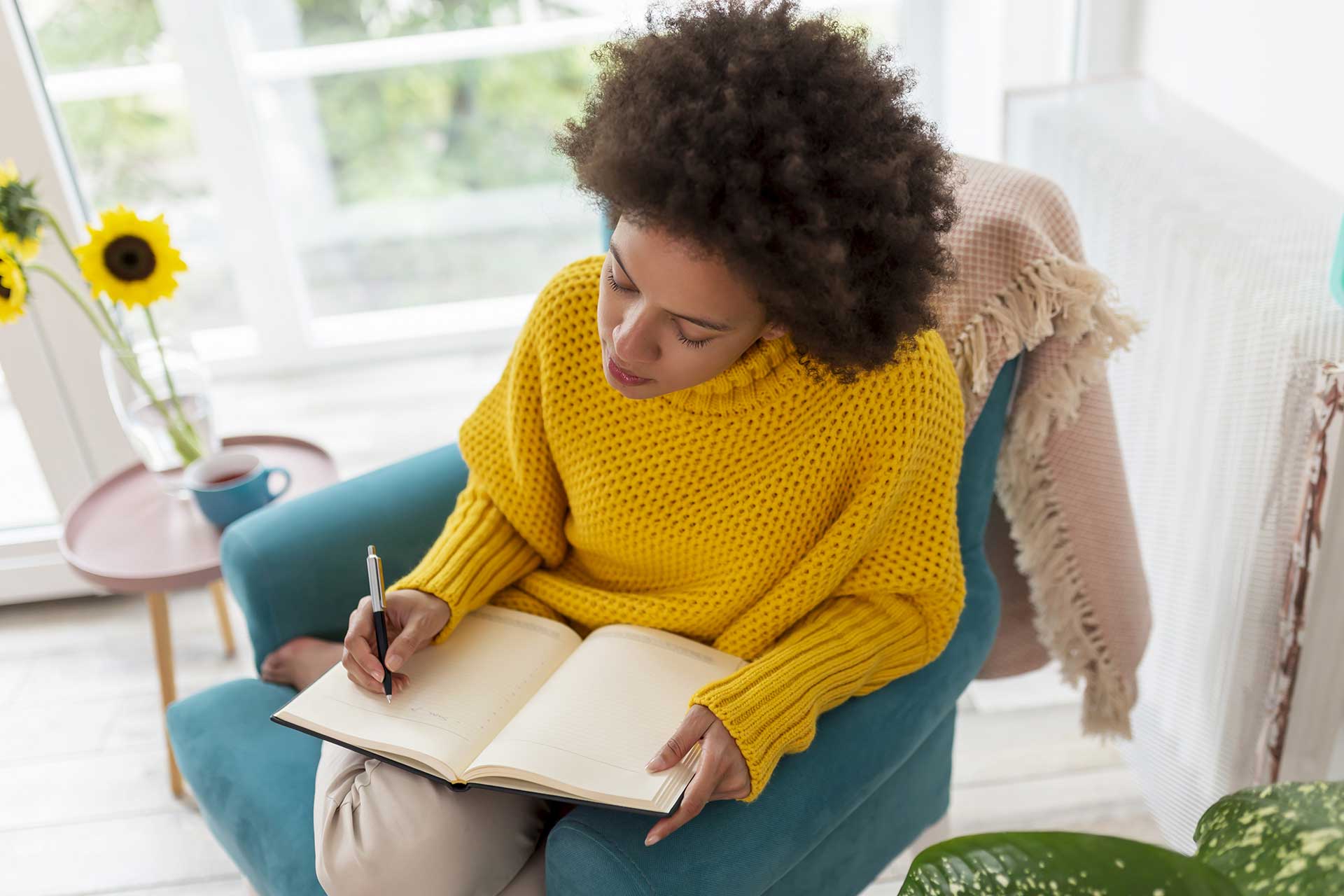 Woman writing in journal in a sunny room.
